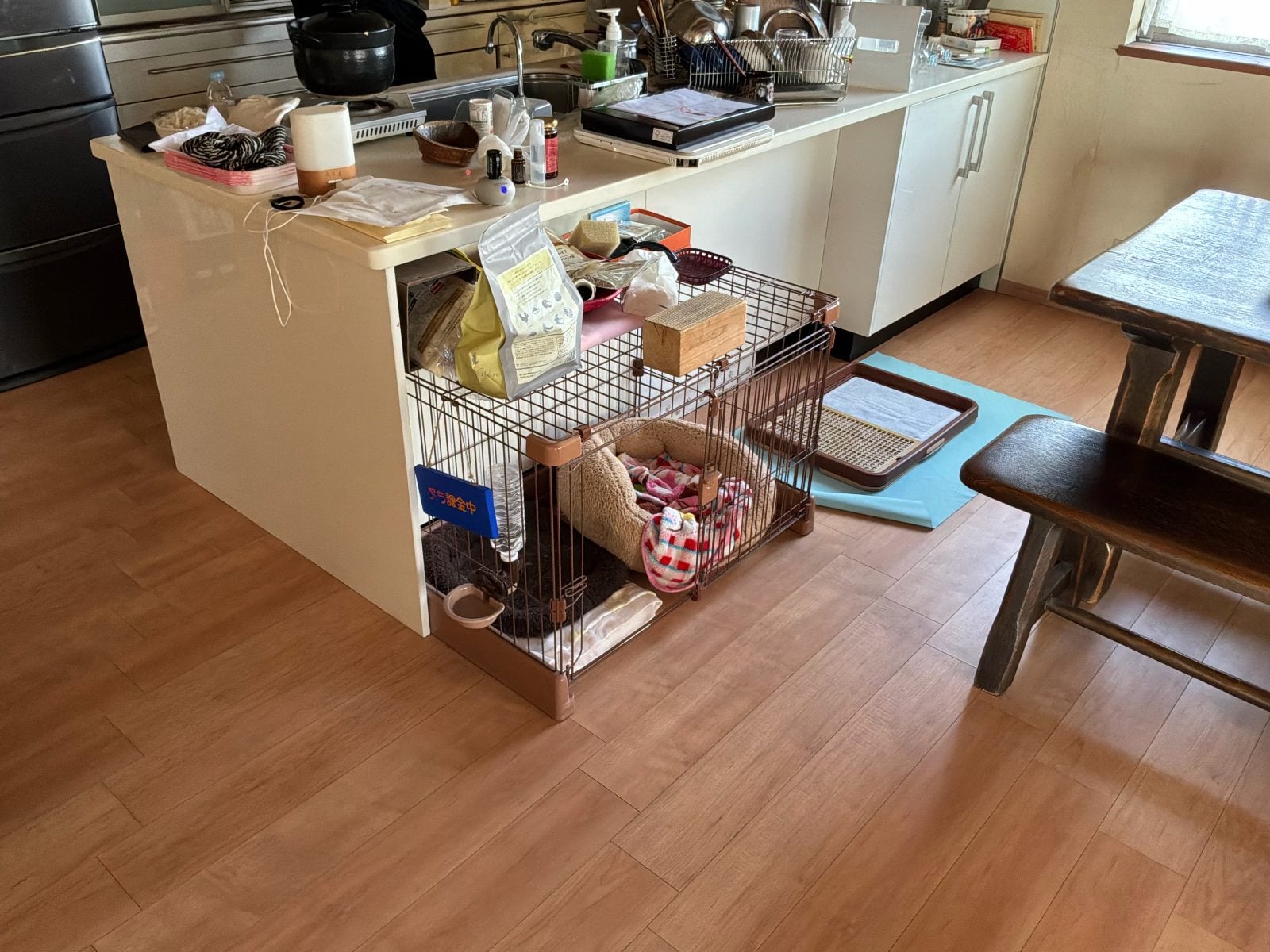 K様邸リフォーム前のキッチン全景。既存の対面型カウンターとペットケージが置かれた状態です。