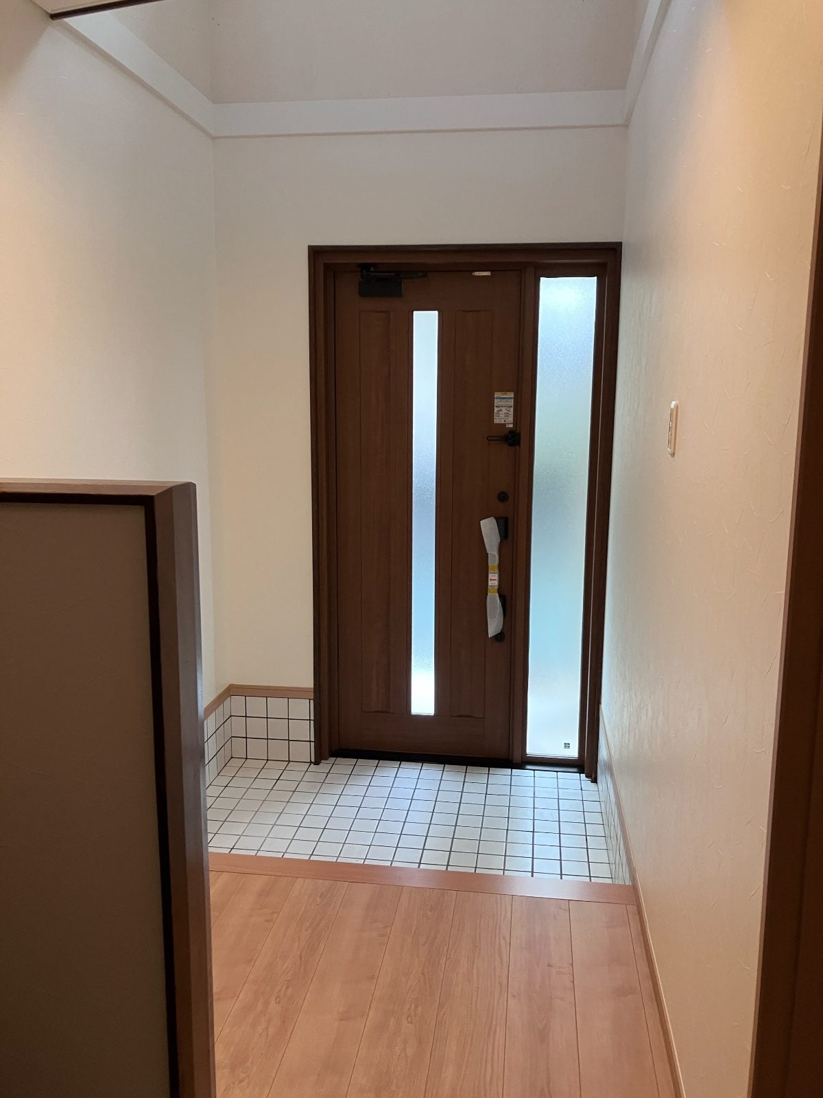 M様邸玄関ホール内側から玄関ドアを望む。白いクロスとタイル土間が明るく清潔な印象を与えます。