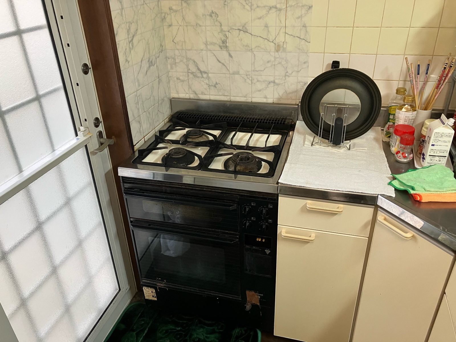 M様邸キッチンリフォーム前。既存のガスコンロ・オーブンレンジとタイル壁の状態を記録した施工前写真です。