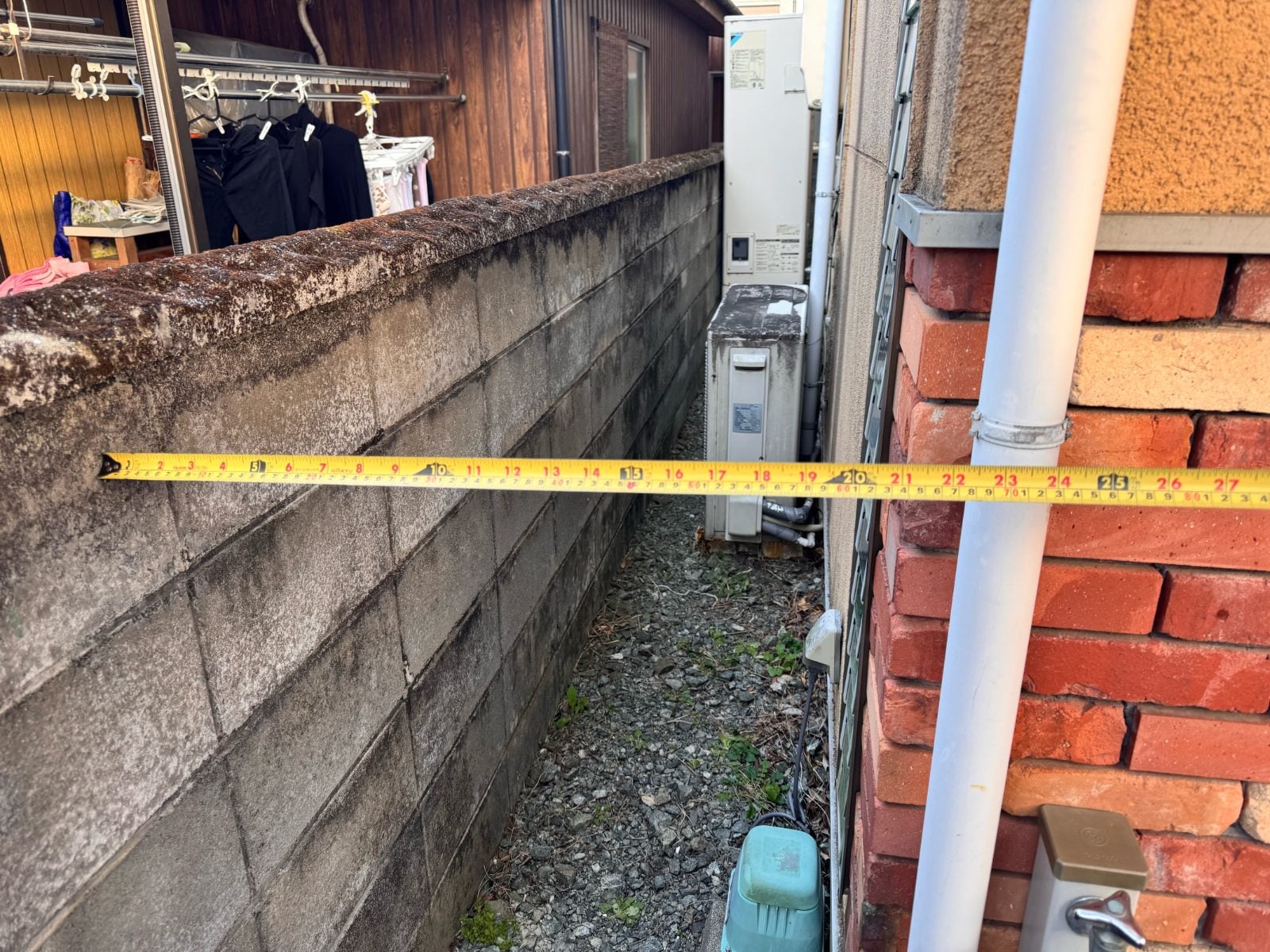 M様邸施工前の外壁側面通路をメジャーで実測している様子。狭小スペースの寸法確認写真です。